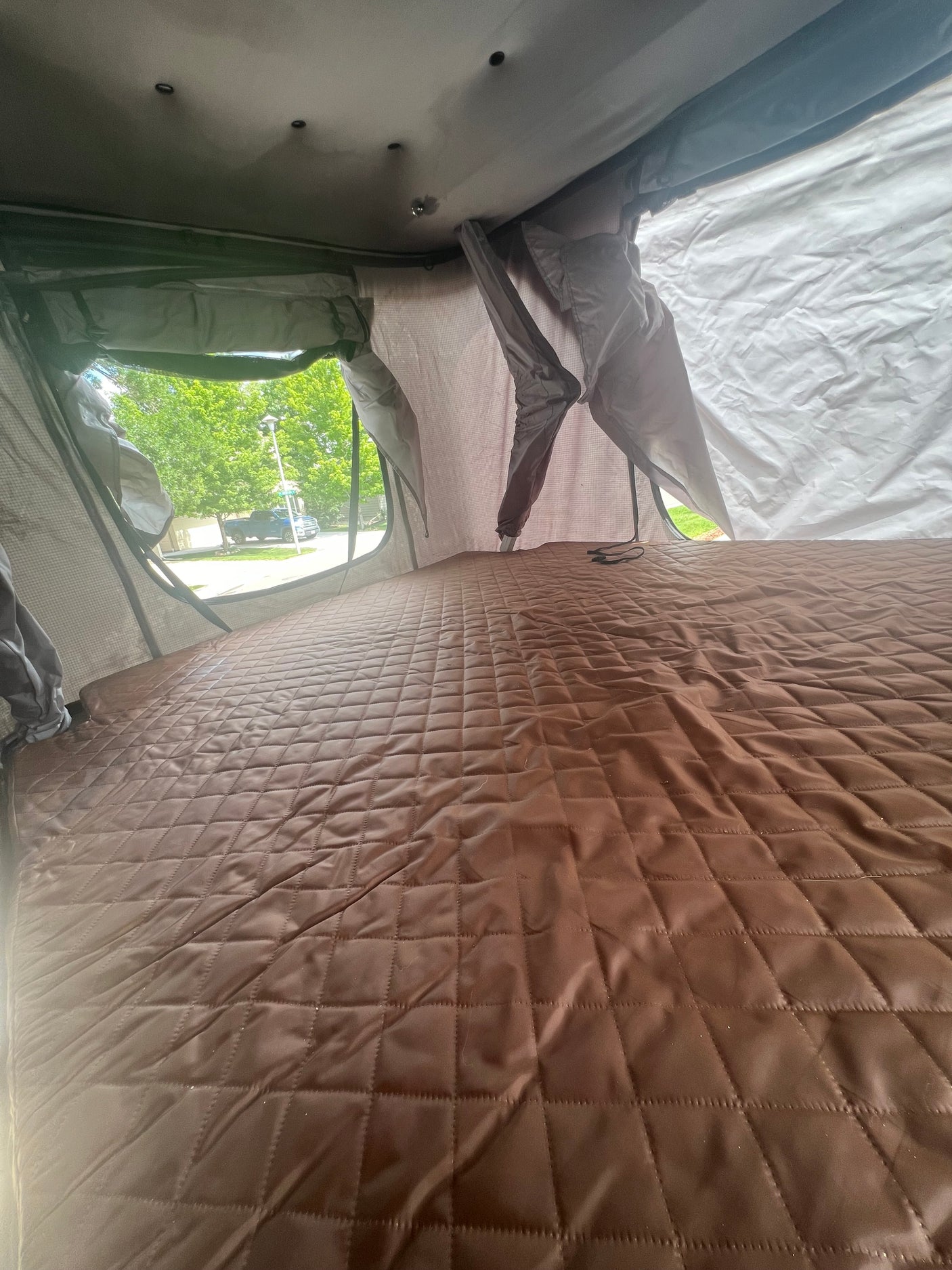 View from inside an RV rental rooftop tent, featuring a quilted mattress and outdoor street view.