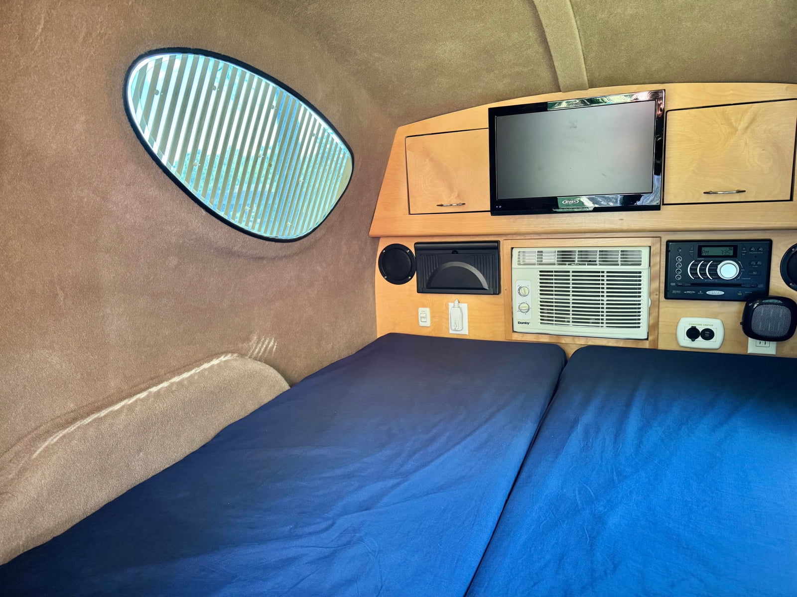 RV rental interior: two beds with blue sheets, a Jensen TV, Danby AC, and stereo system. Cozy space for travel.
