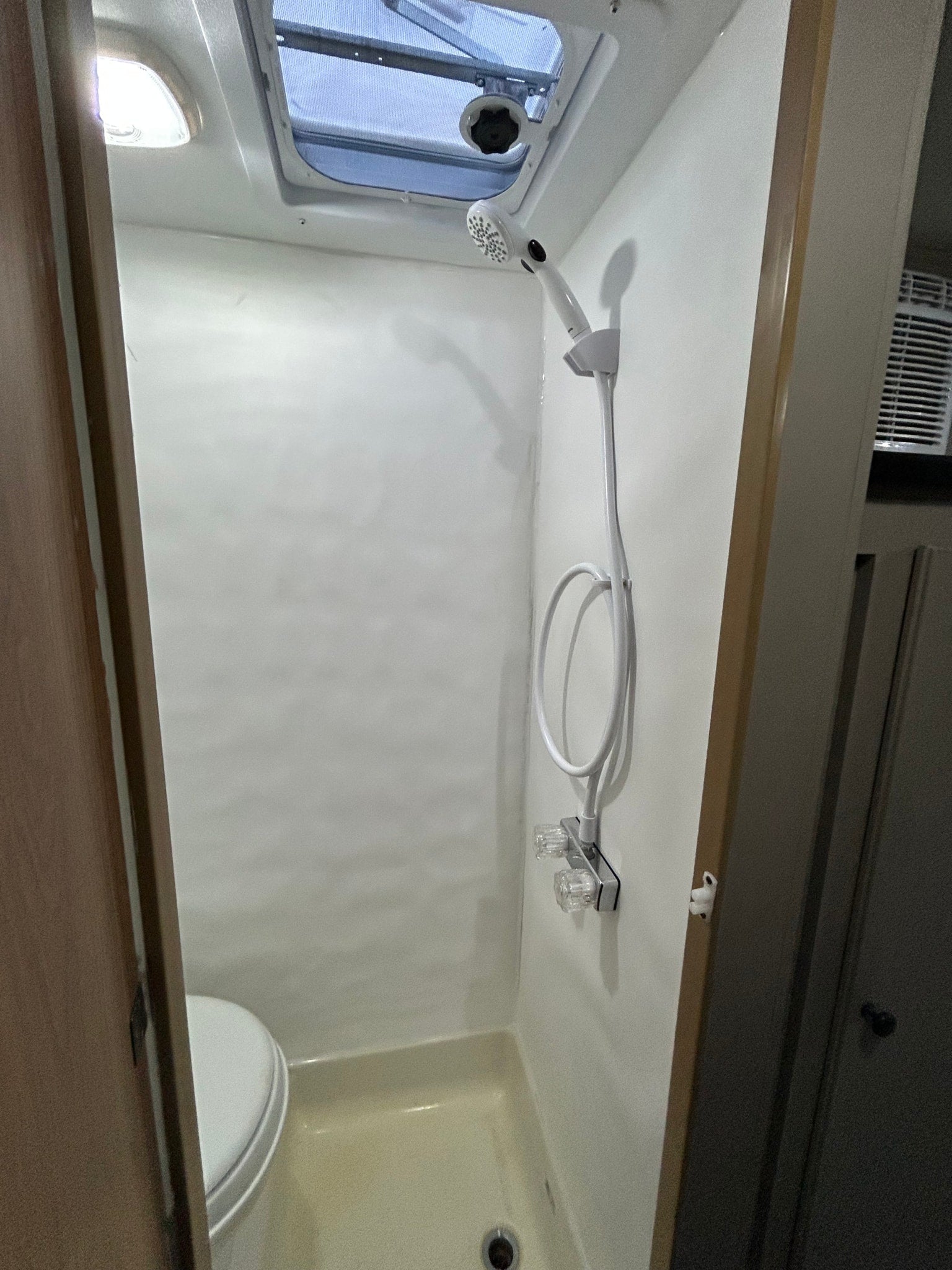 RV rental wet bath: compact space featuring a shower, toilet, light, and ceiling vent.