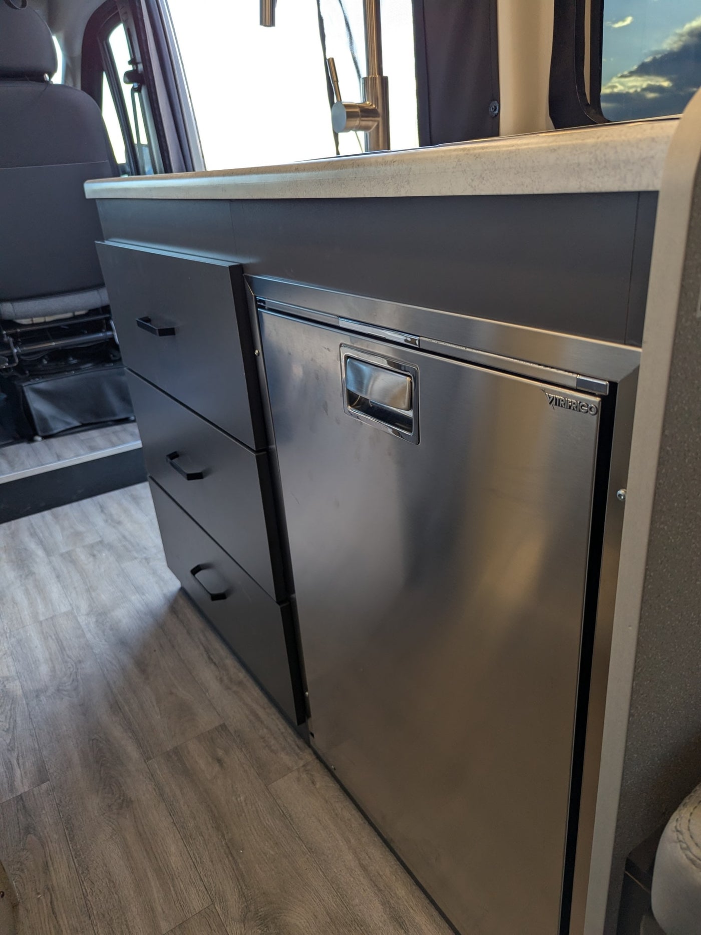 Modern RV rental interior with compact kitchen: countertop, faucet, drawers, and built-in fridge. — photo 9