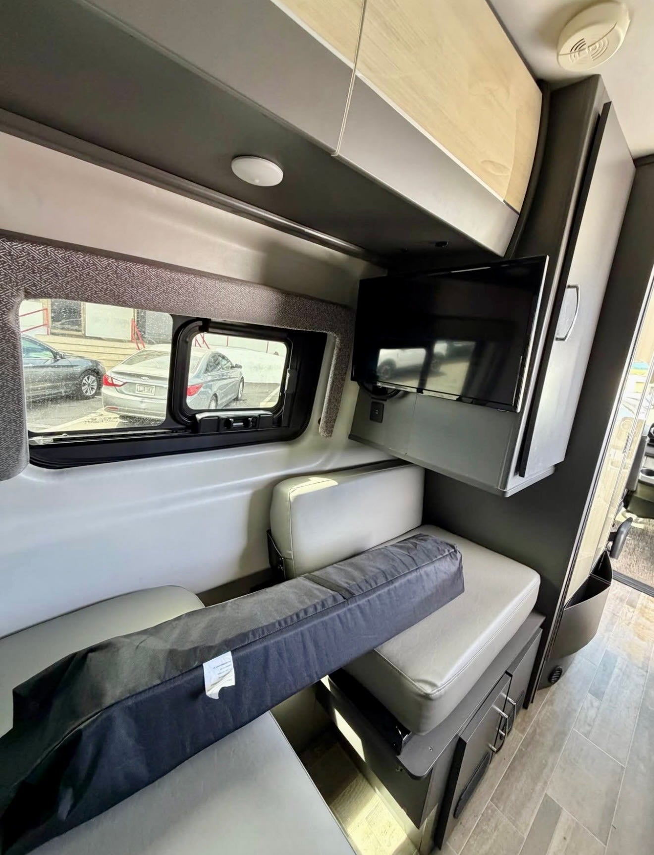 Explore this RV rental's interior: comfy bench seating, windows, and a wall-mounted TV. A black bag rests on the cushions.