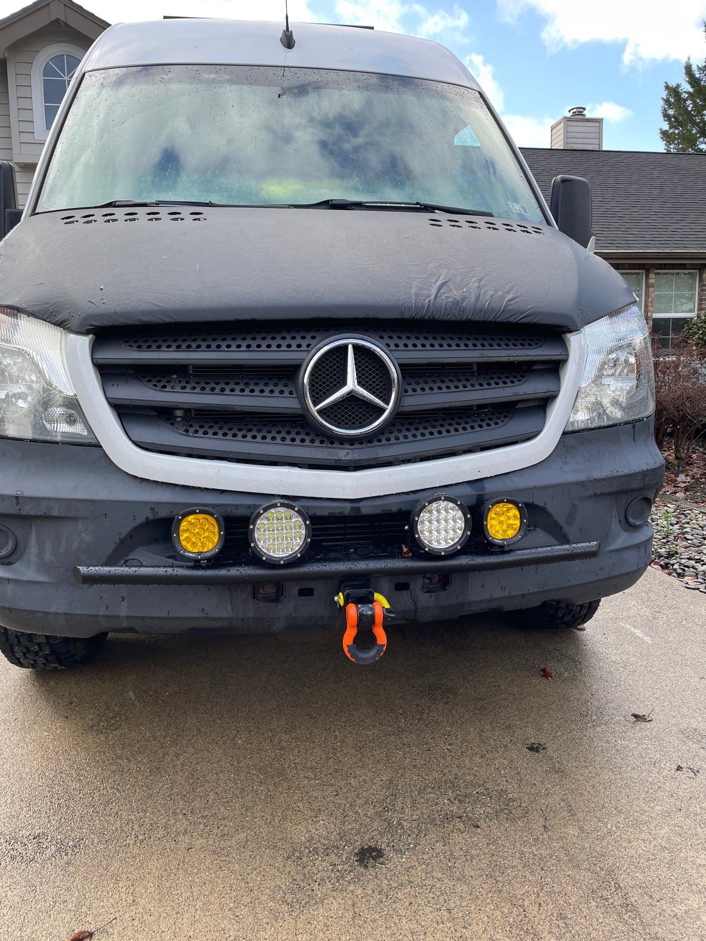Front of a grey Mercedes Sprinter RV rental van. Features auxiliary lights, tow shackle, and a dark hood cover.