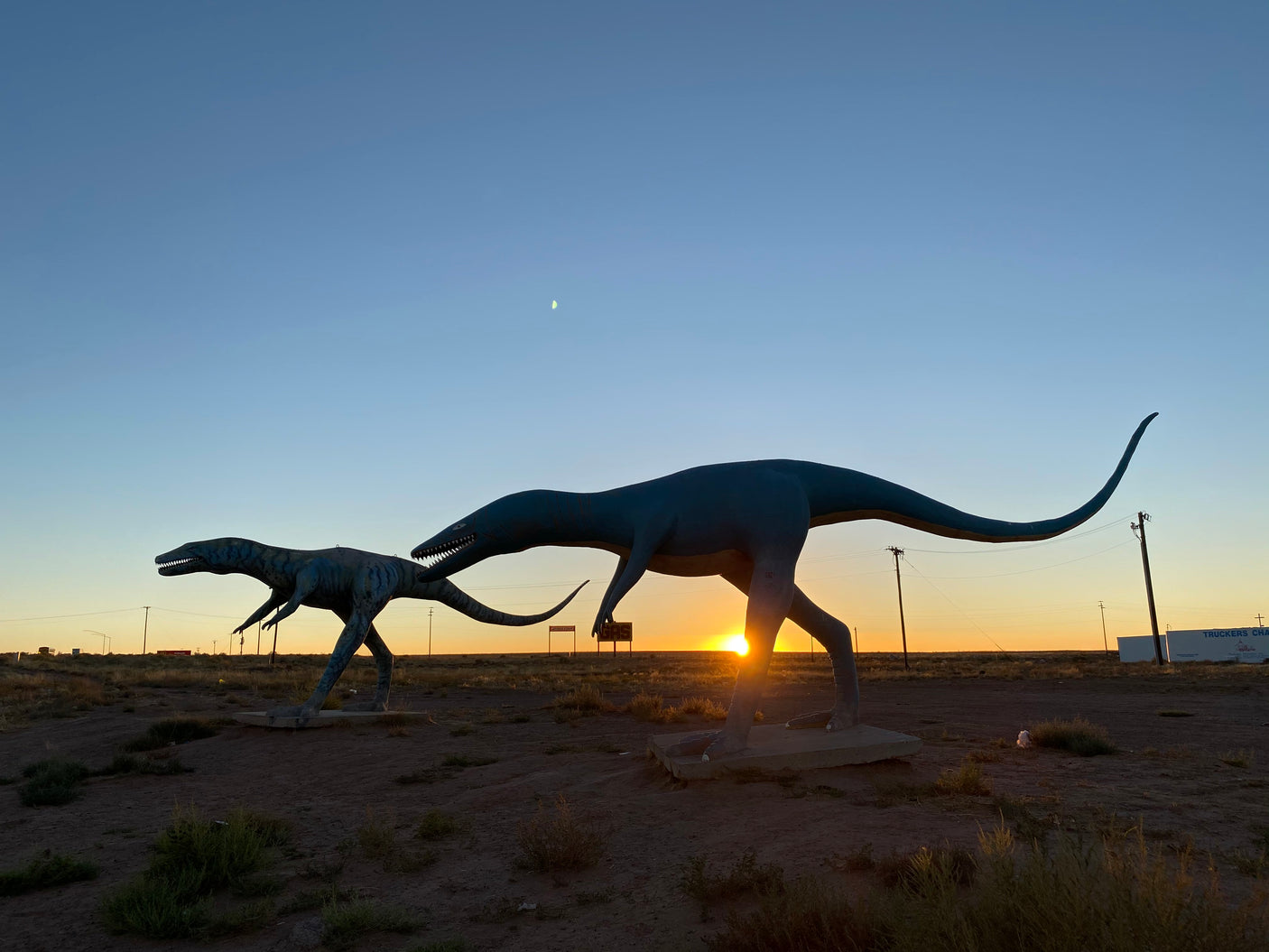 Iconic dinosaur statues silhouetted by sunset & moon. A memorable stop for your RV rental journey through the desert.