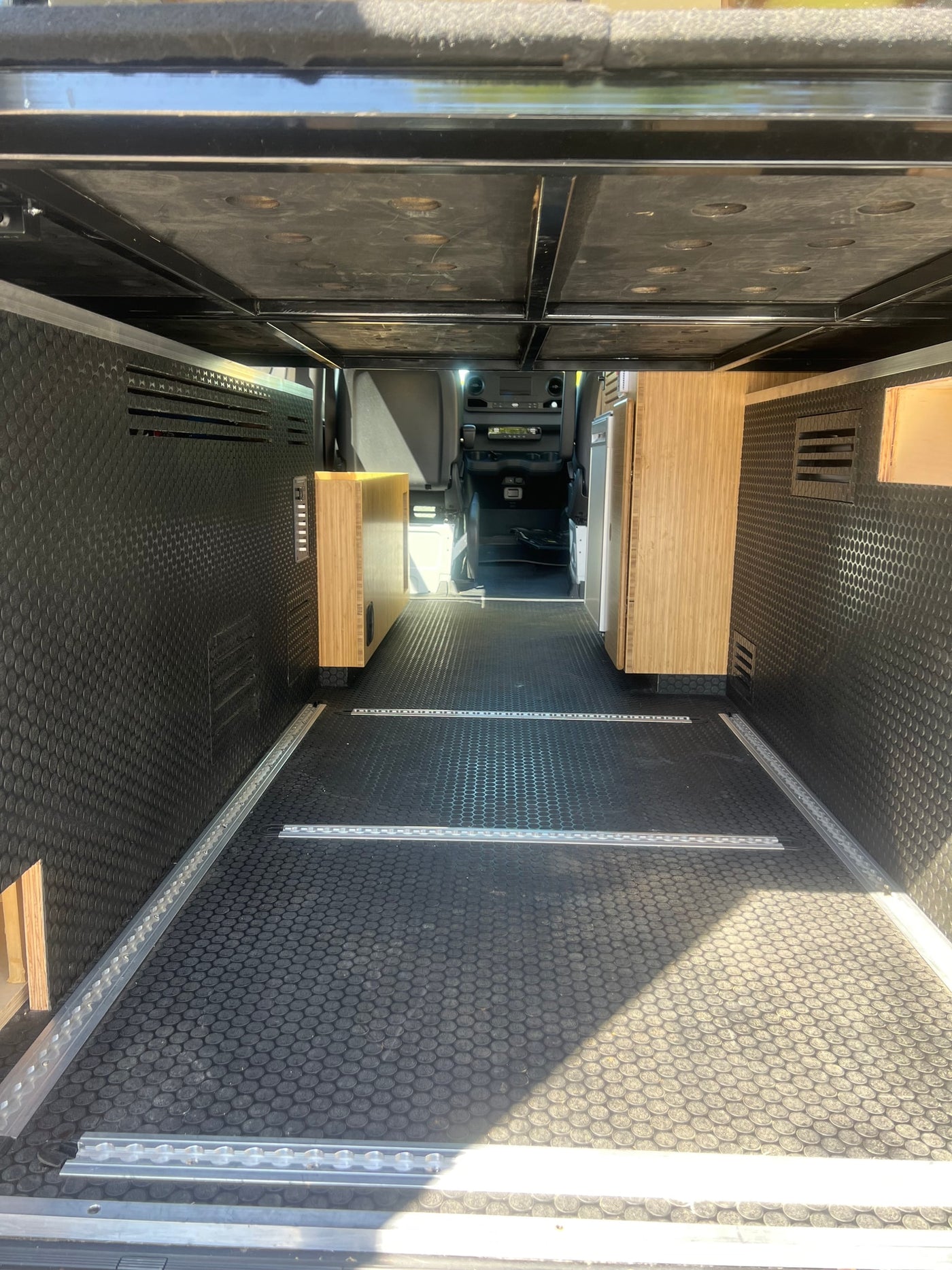 Interior of an RV rental camper van: elevated bed platform, wooden cabinetry, and L-track flooring for versatile storage. — photo 19