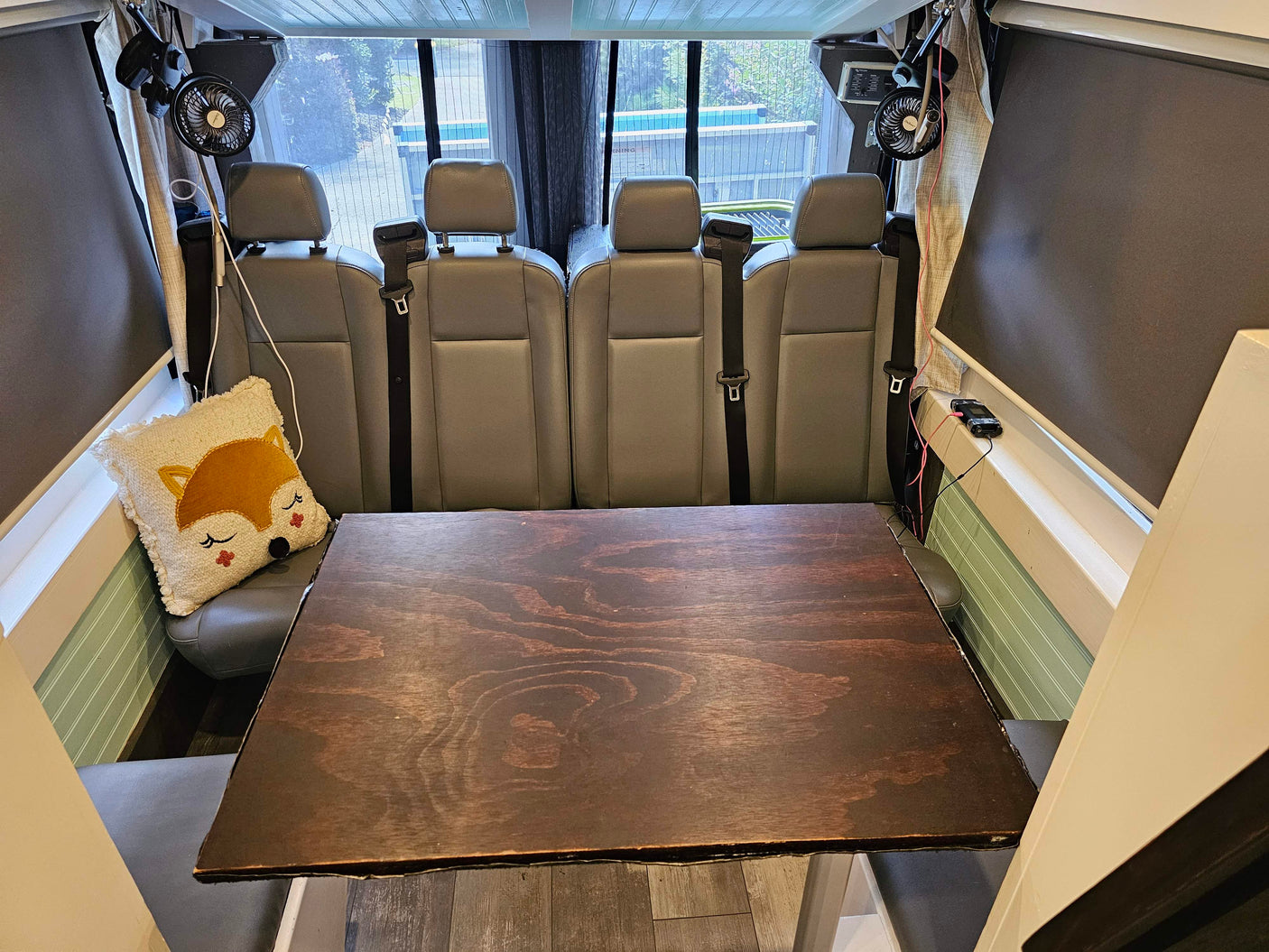Cozy RV rental interior with four comfy seats, a large wooden table, and fans. Ideal setup for dining or work on your next adventure!
