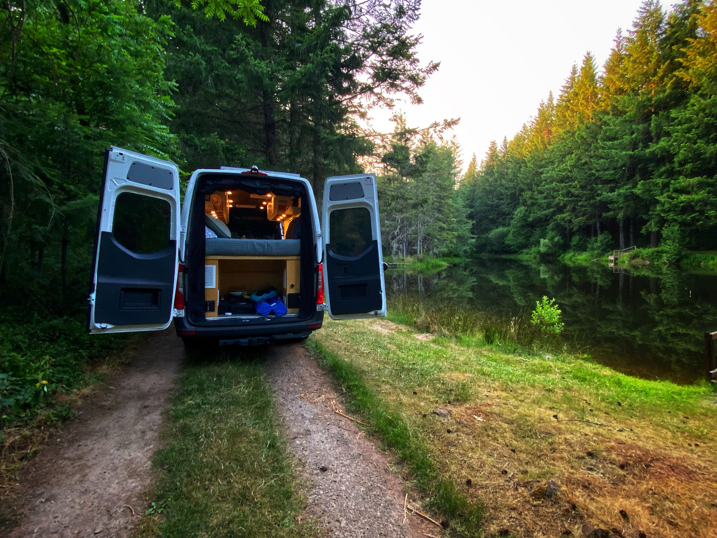 Cozy rv rental camper van parked by a peaceful, tree-lined lake, revealing a comfortable interior for outdoor travel.