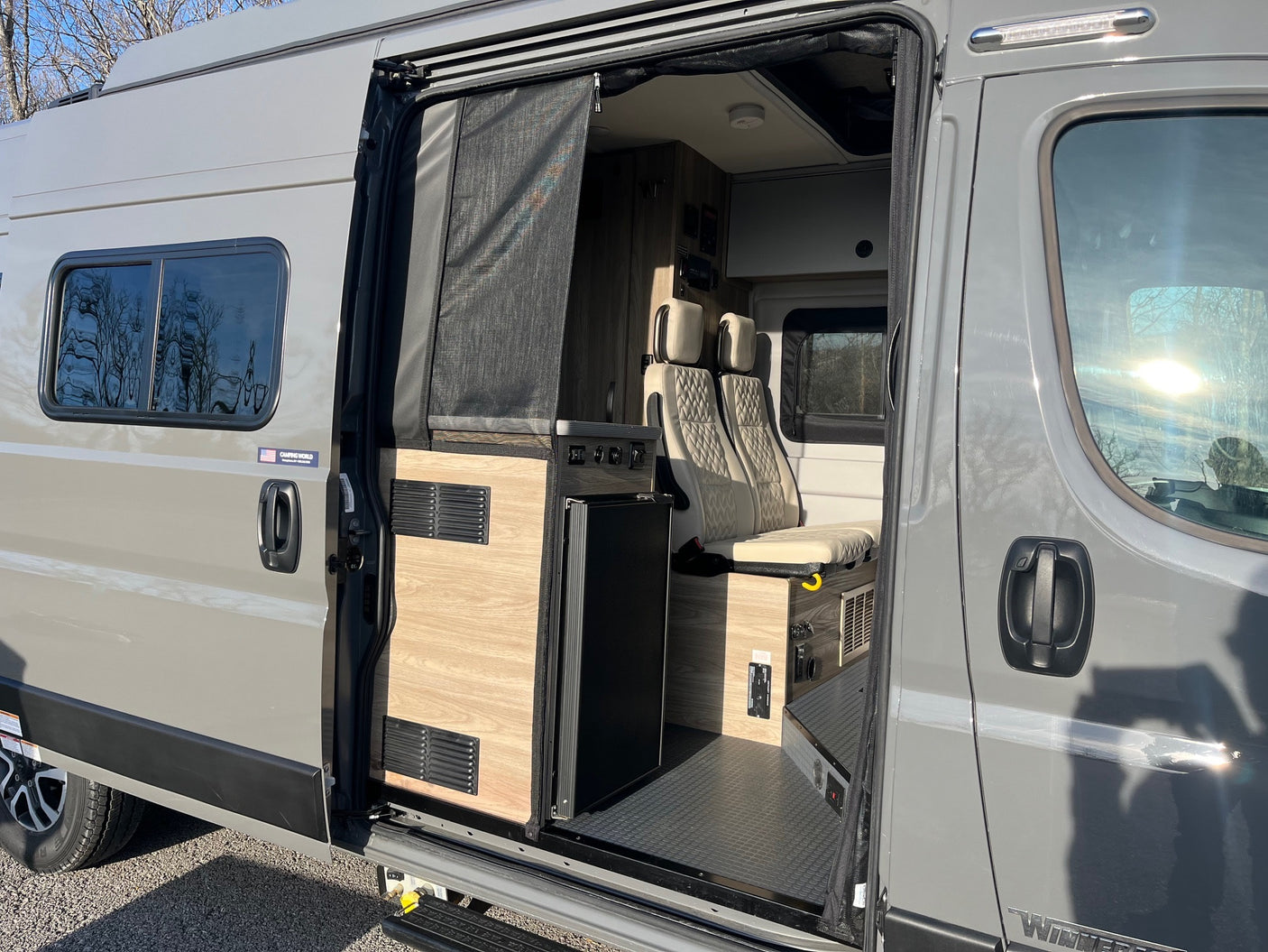 Modern rv rental camper van, side view with open door. See inside: kitchenette, passenger seats, and outside details.
