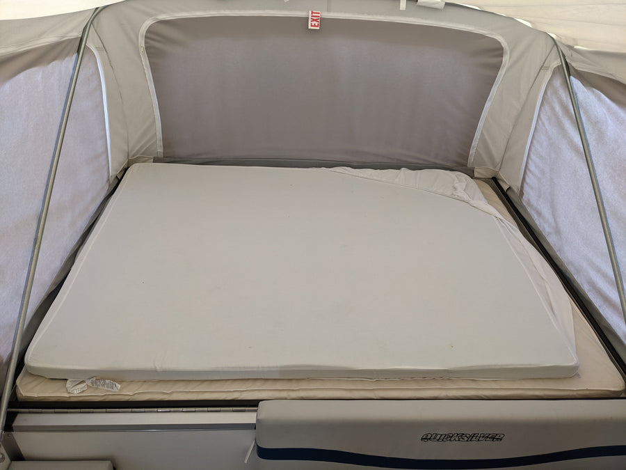 RV rental pop-up camper's interior bed: layered mattresses with an "EXIT" sign above. Quicksilver branding visible.