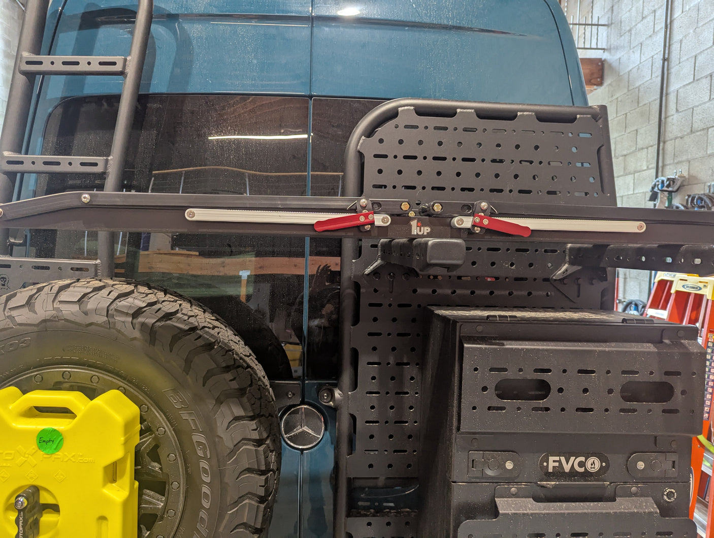 Rear of a Mercedes-Benz rv rental van, equipped with an overland bike rack, spare tire, ladder, and gear storage.