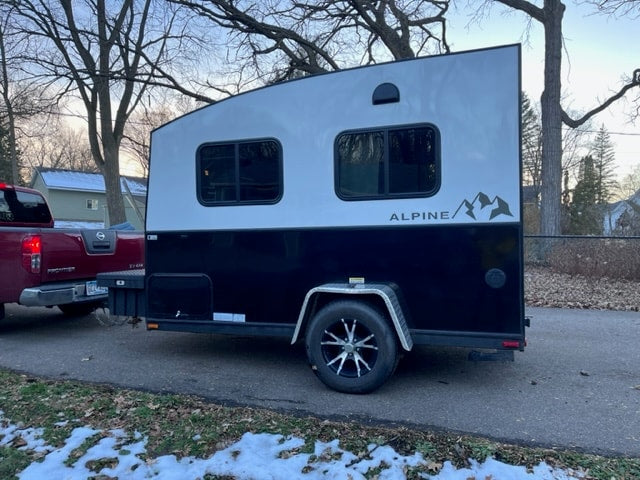 A compact black and white Alpine camper trailer, hitched to a red pickup truck, ready for your next RV rental adventure.