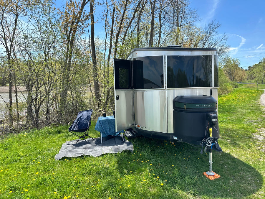 A silver Airstream travel trailer (RV rental) with an outdoor seating area by a pond on a sunny day.