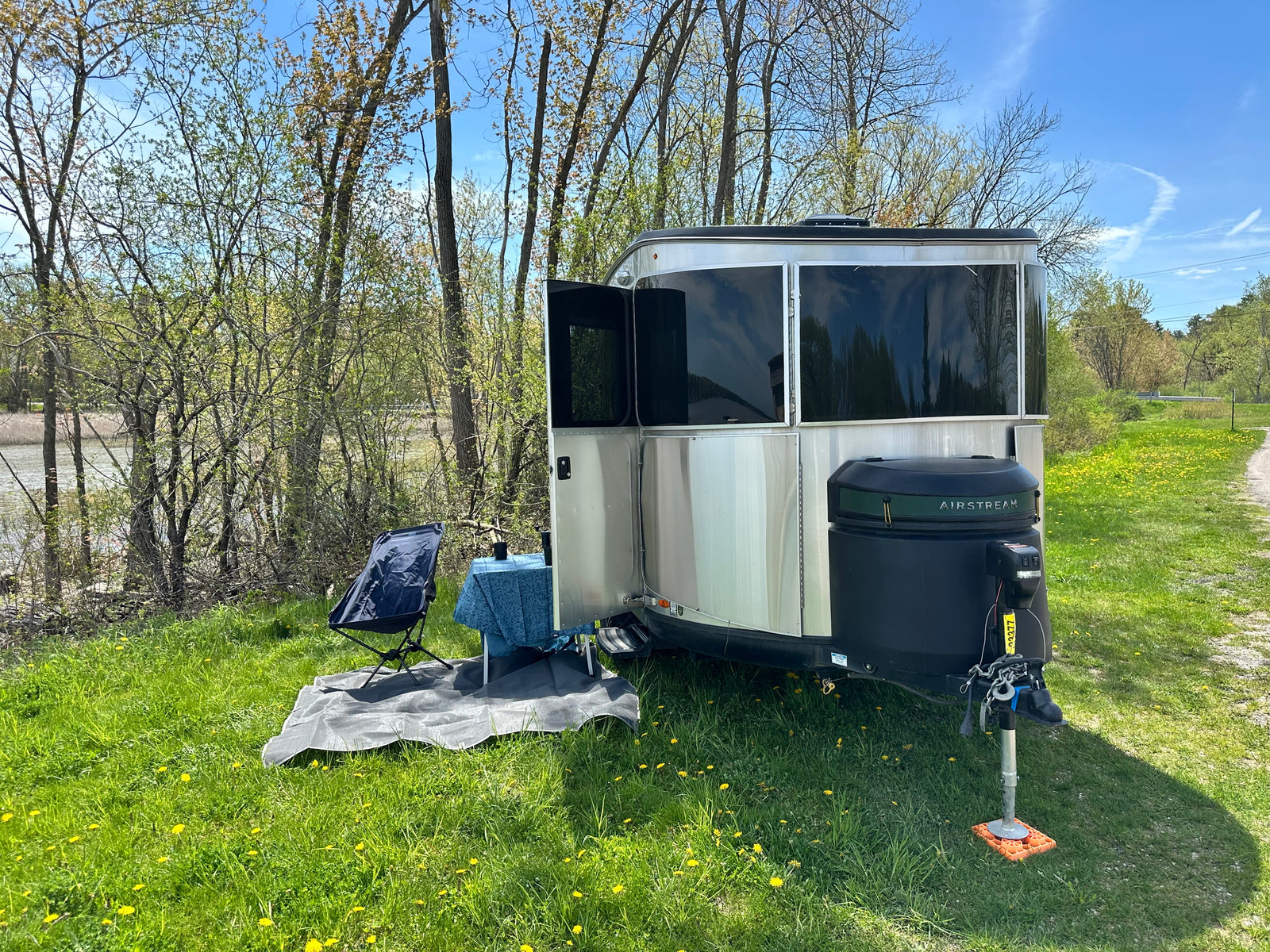 A silver Airstream travel trailer (RV rental) with an outdoor seating area by a pond on a sunny day.