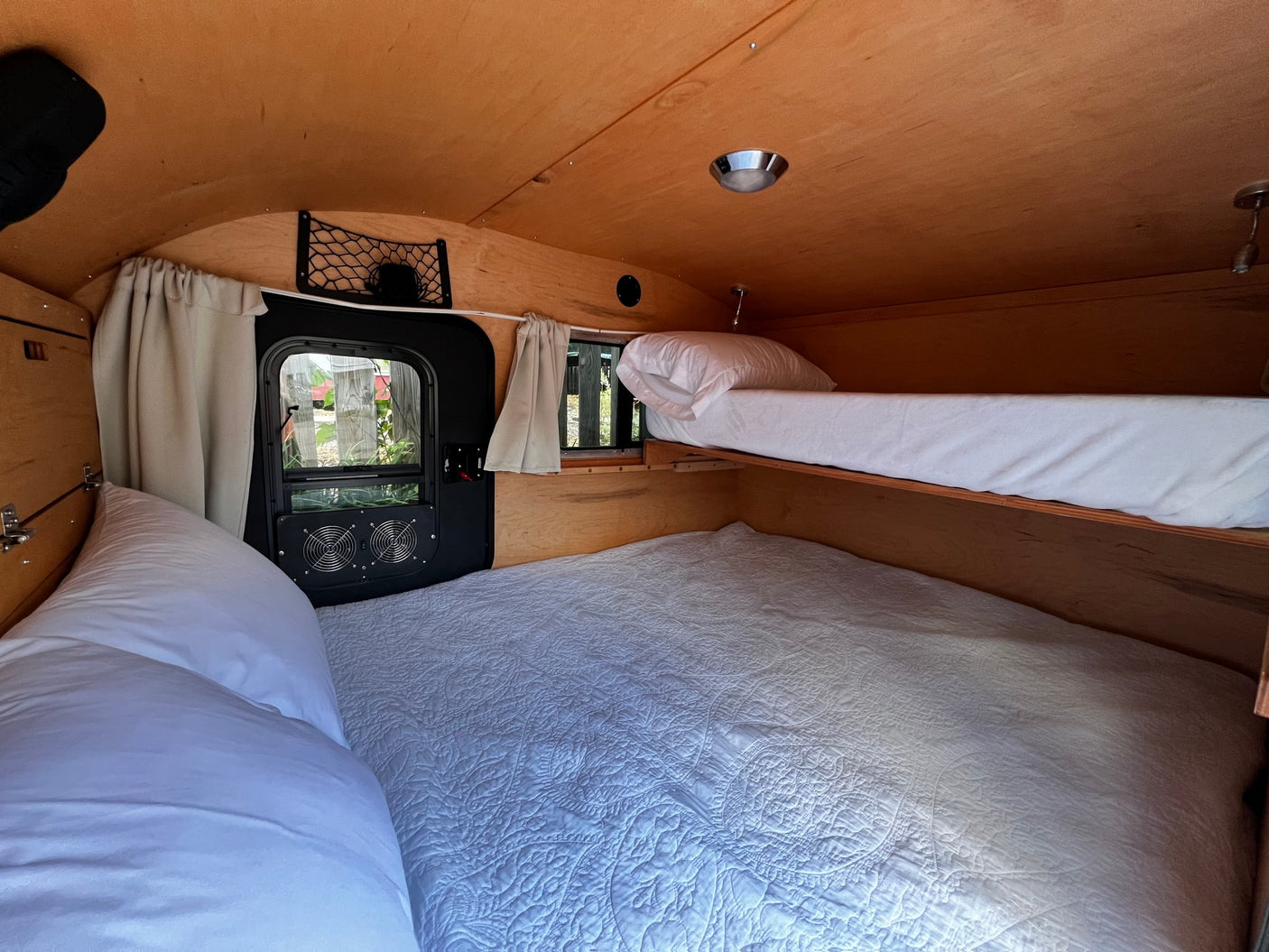 Cozy RV rental interior with wooden walls and ceiling, featuring comfortable bunk beds, a window, and fans for comfort.