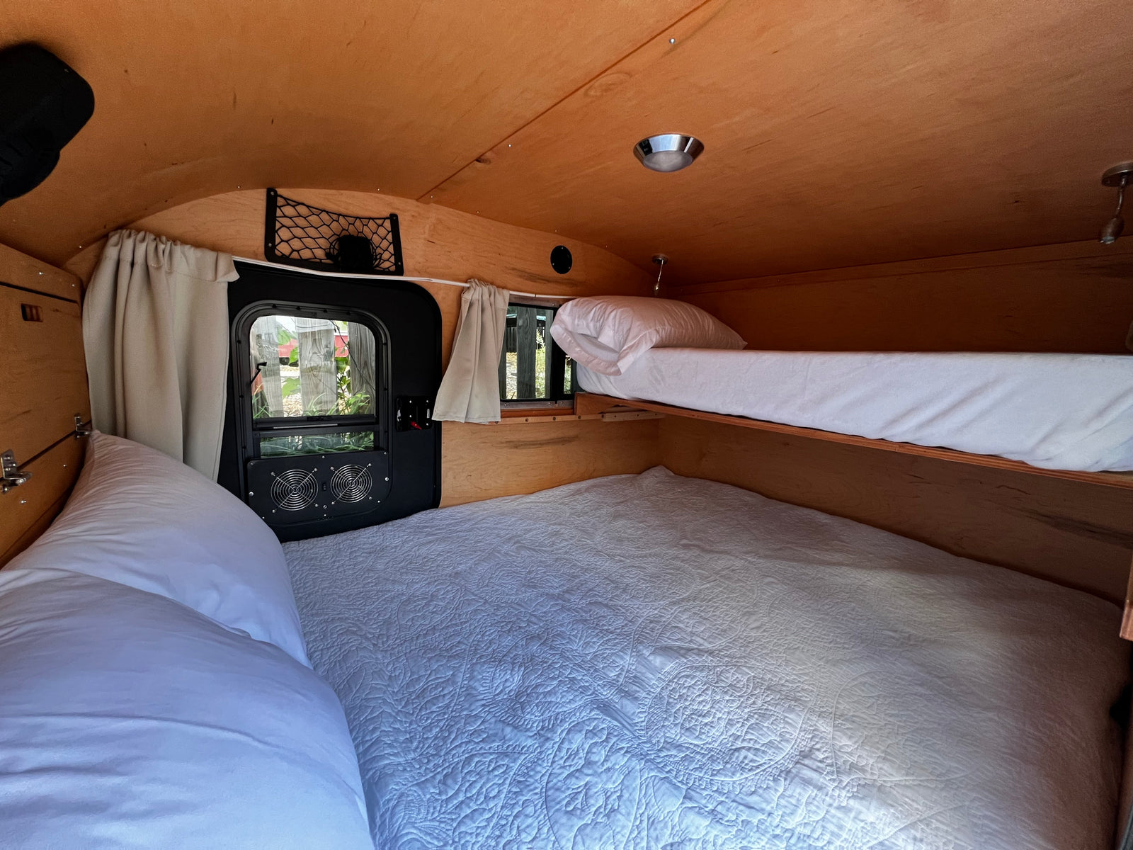 Cozy RV rental interior with wooden walls and ceiling, featuring comfortable bunk beds, a window, and fans for comfort.