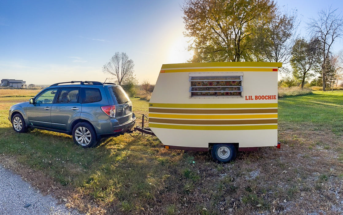 An inviting view of a blue Subaru Forester SUV towing a charming, retro "LIL BOOCHIE" camper, hinting at a fun rv rental journey.