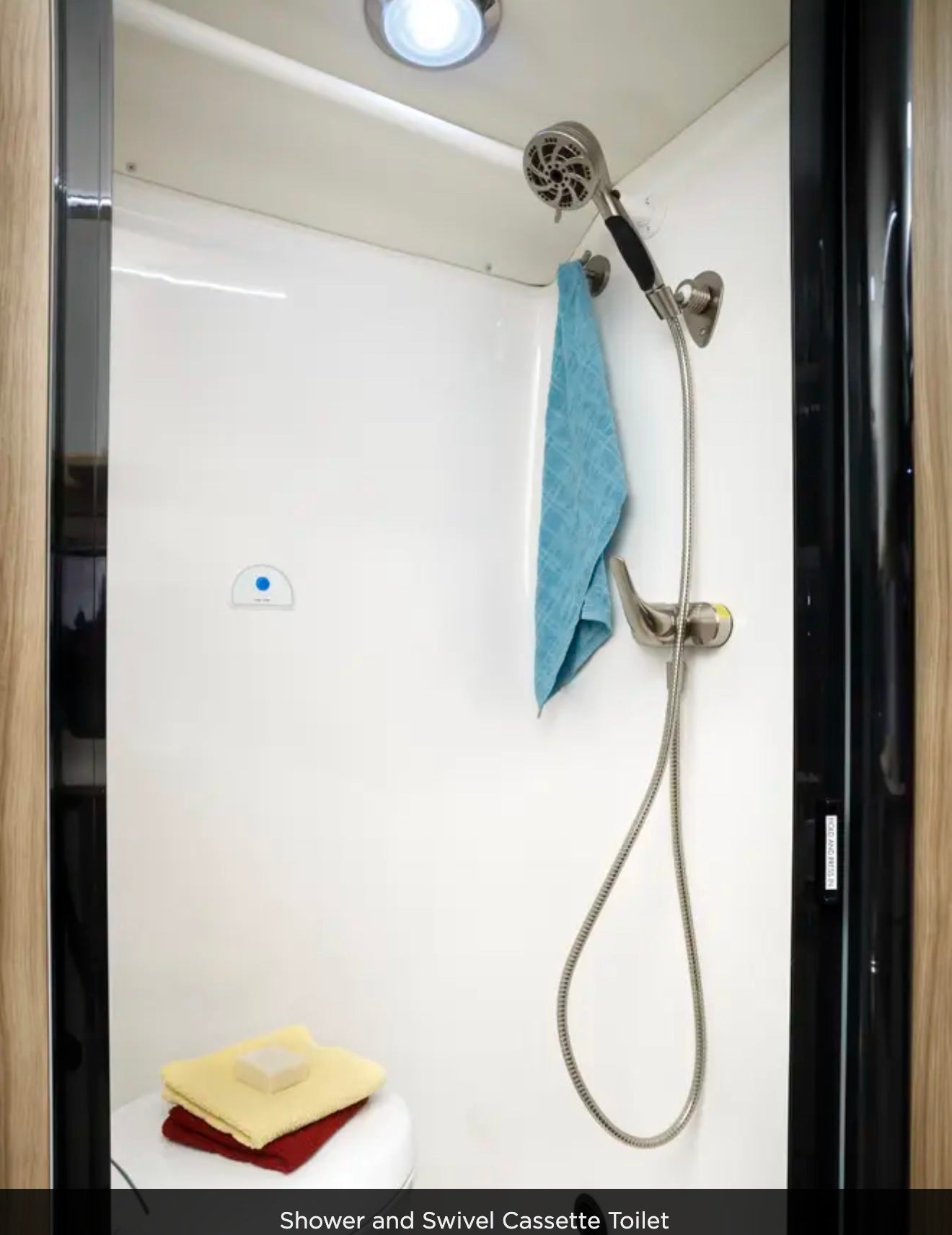 Compact RV rental bathroom: shower, blue towel, and swivel cassette toilet with soap & towels.