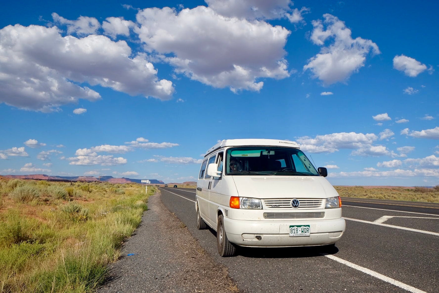 Enjoying the view from a white camper van RV rental on a desert road trip. Blue sky, clouds, and distant mountains.
