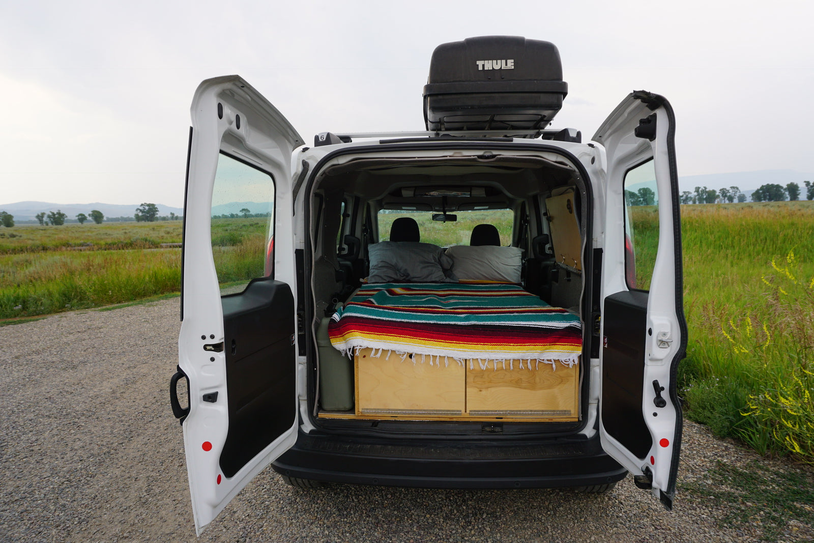 This camper van interior, ideal for an rv rental, features a bed, storage, and Thule roof box, ready for nature adventures.