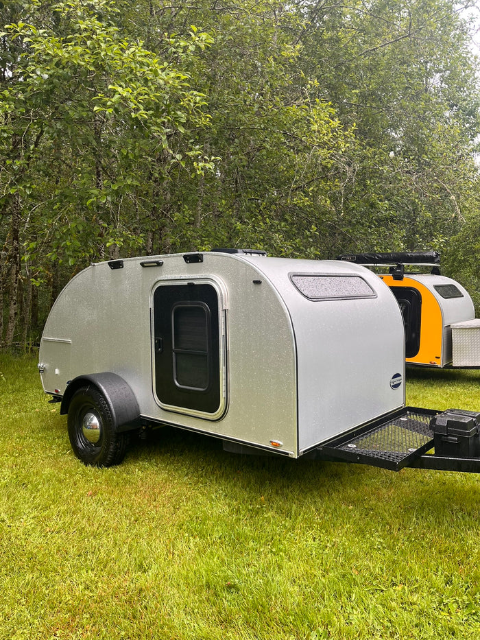 perfect for your next RV rental trip.|Silver and orange teardrop rv rental campers sit on wet grass among trees. Compact RVs perfect for your next outdoor adventure.|Cozy RV rental: a plush bed