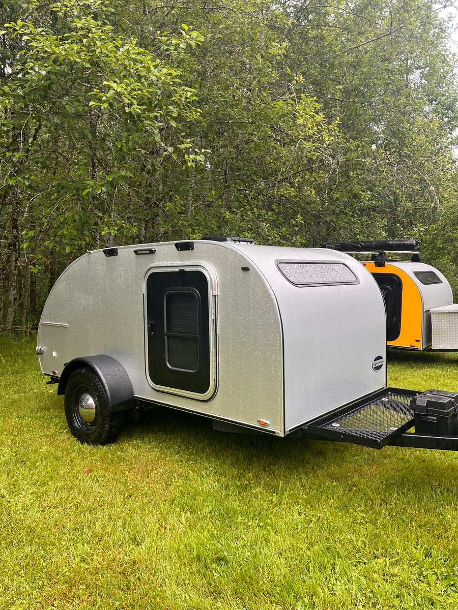 perfect for your next RV rental trip.|Silver and orange teardrop rv rental campers sit on wet grass among trees. Compact RVs perfect for your next outdoor adventure.|Cozy RV rental: a plush bed