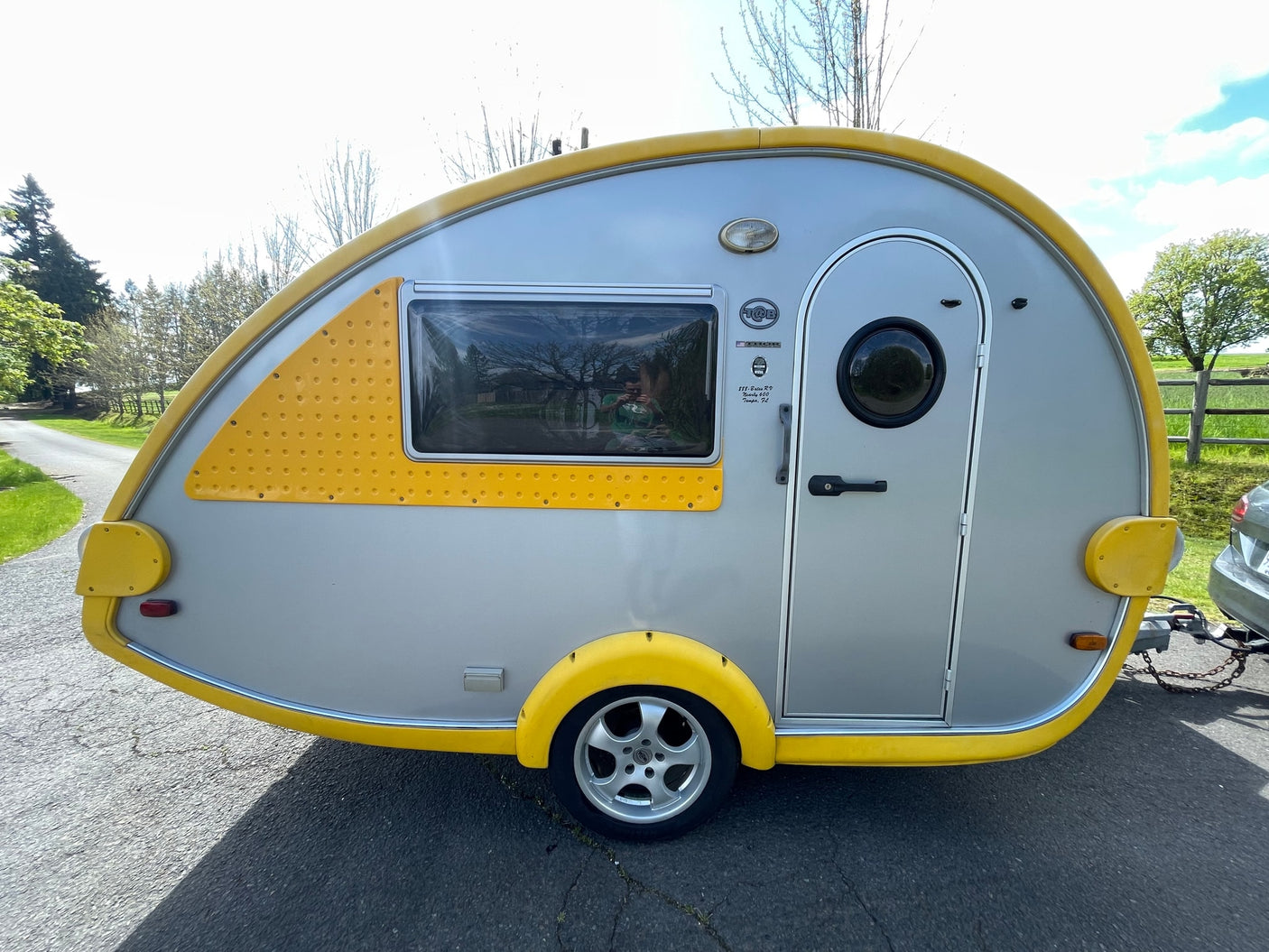 Side view of a compact, yellow and grey teardrop travel trailer, perfect for an RV rental or camping adventure.