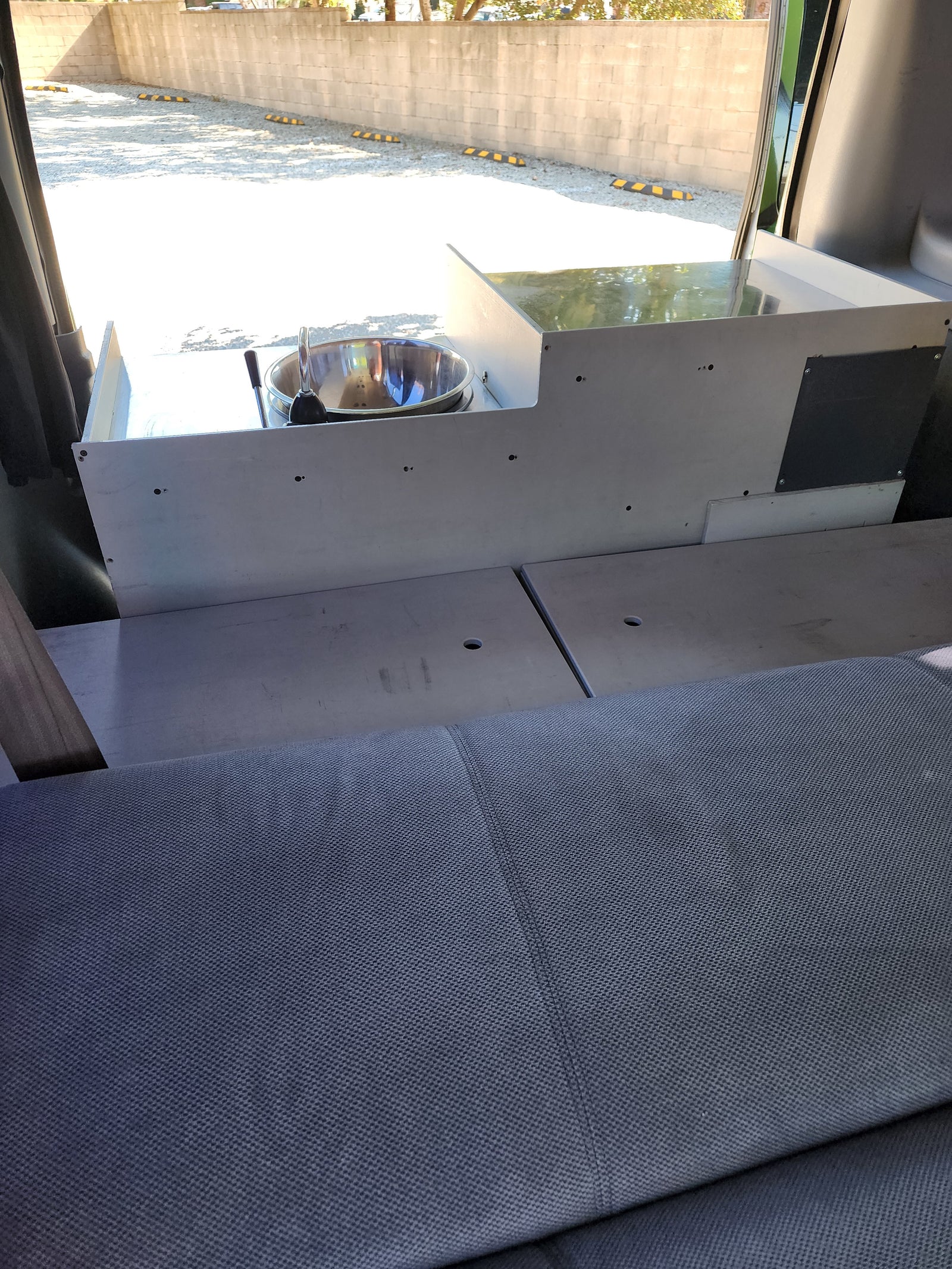 RV rental interior with a custom-built unit featuring a stainless steel sink and faucet, alongside gray fabric seating or a bed.