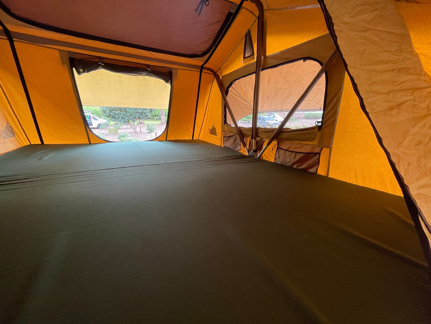 Comfortable sleeping space inside an RV rental rooftop tent, featuring a large green mattress and clear outdoor views.