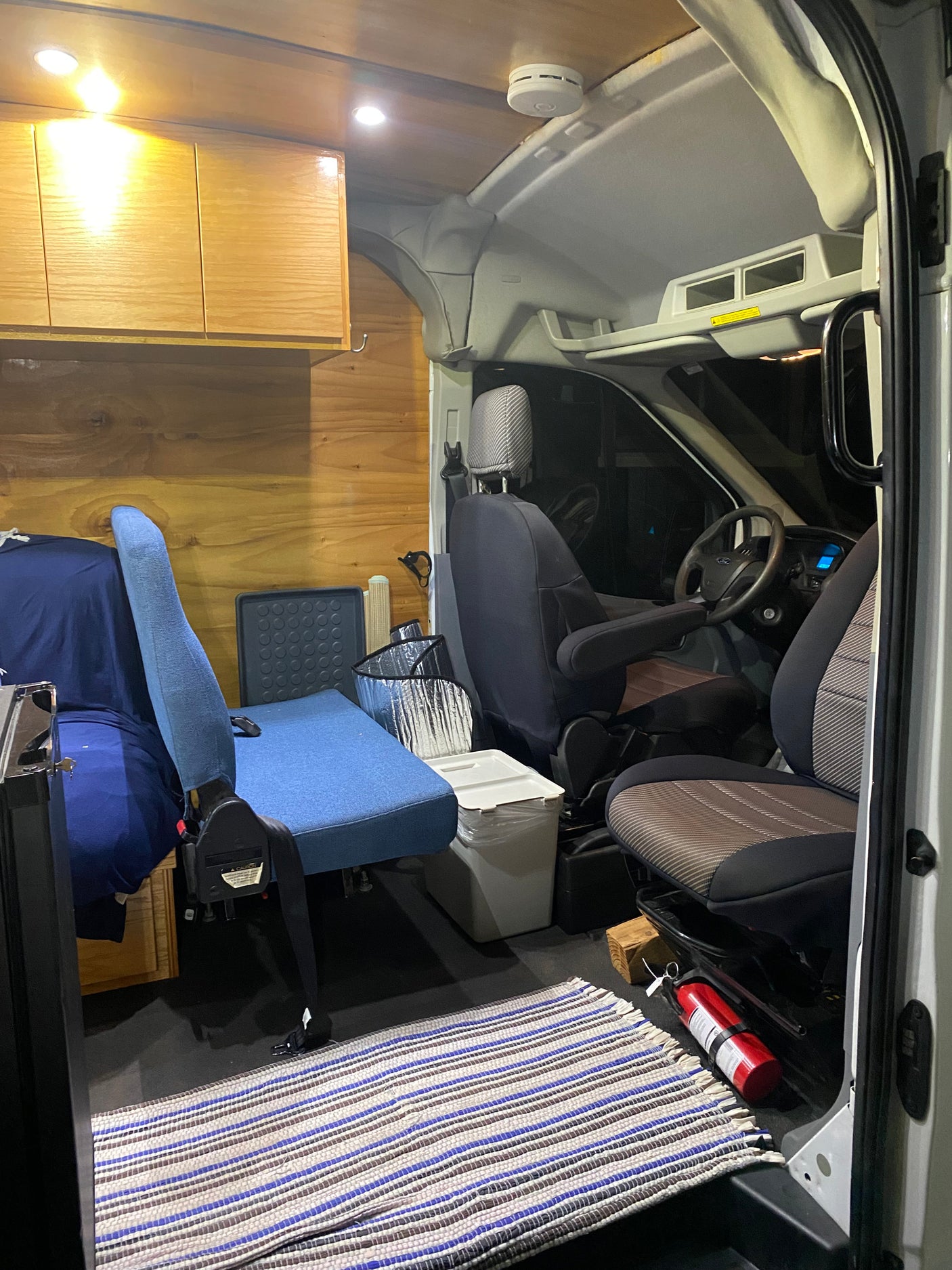 An RV rental interior featuring warm wood, comfortable seating, overhead storage, and safety essentials like a fire extinguisher.