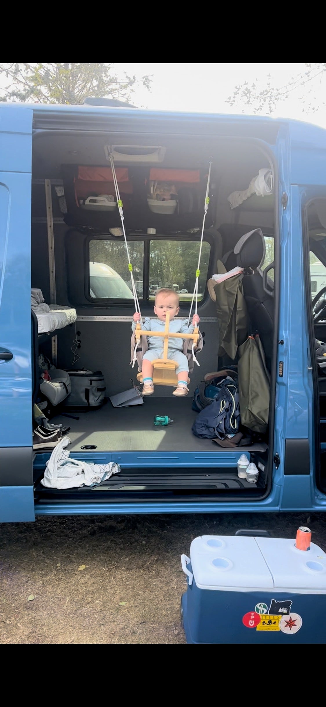 Little one swings inside a blue RV rental van, showcasing family-friendly travel. Perfect for van life adventures!