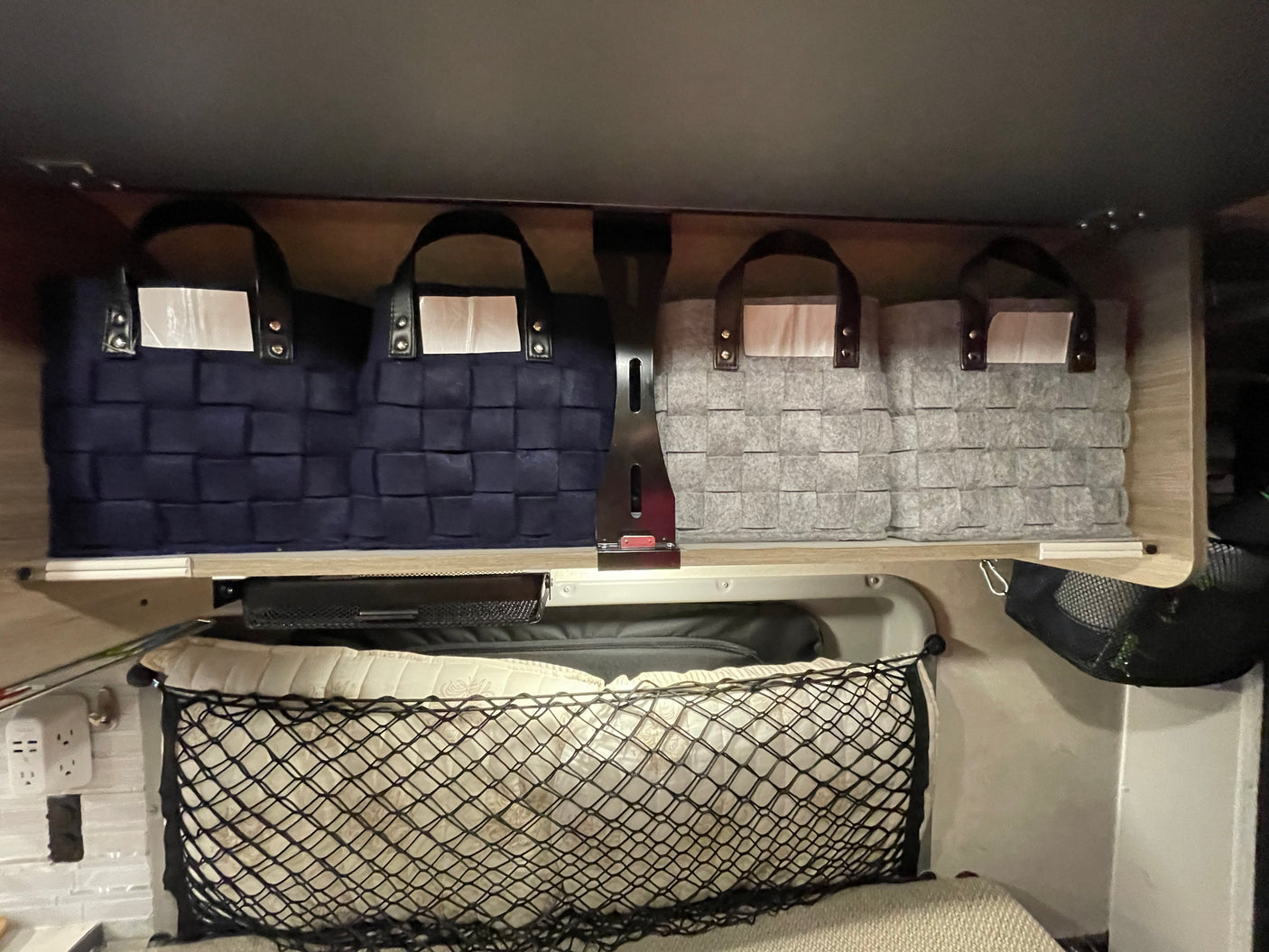 RV rental interior features organized storage: blue & grey woven bins on upper shelf, mesh net below for soft items.
