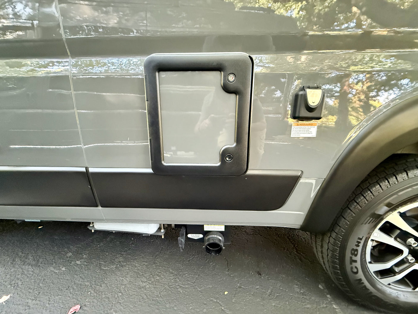 Side of an RV rental, showing a utility access panel, electrical inlet, and gray water tank drain valve for waste disposal.