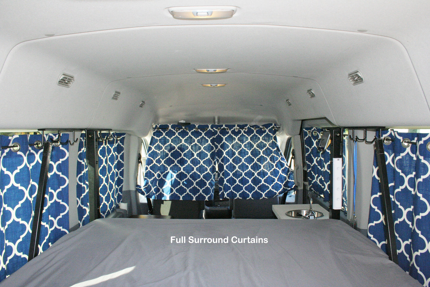 RV rental: Camper van interior featuring a comfortable bed, small sink, and full surround blue patterned privacy curtains.
