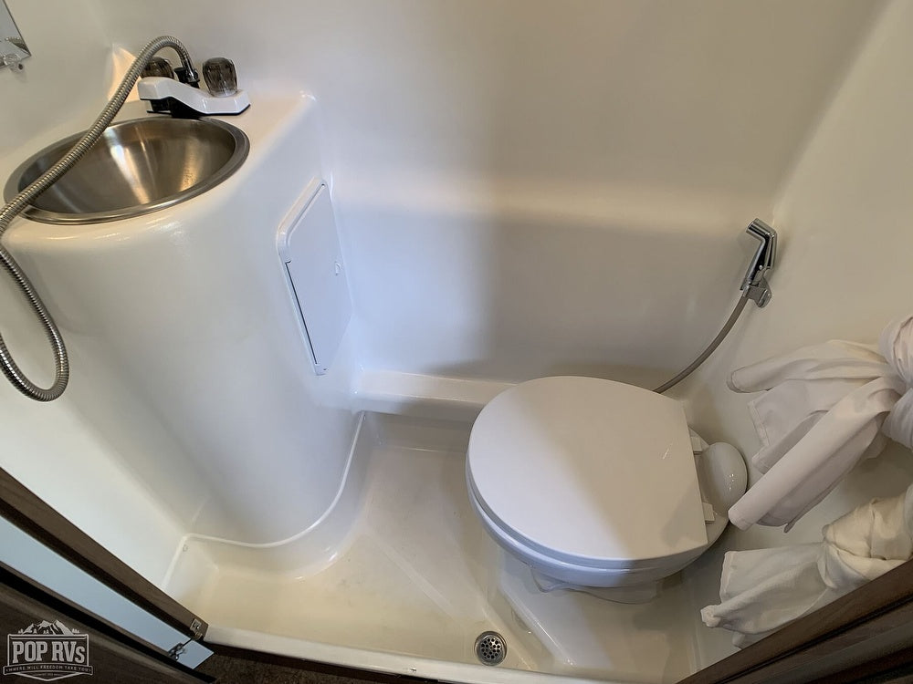 Compact white wet bath in an RV rental, featuring a sink with shower hose, toilet, and floor drain.