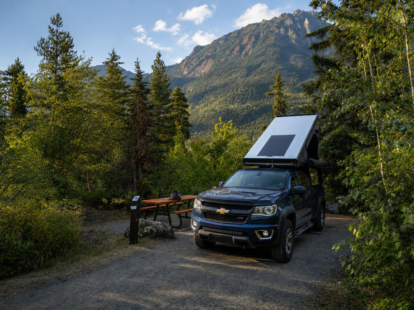 Adventure-ready pickup with rooftop tent & solar panel at a stunning mountain campsite. A unique RV rental option for wilderness exploration!