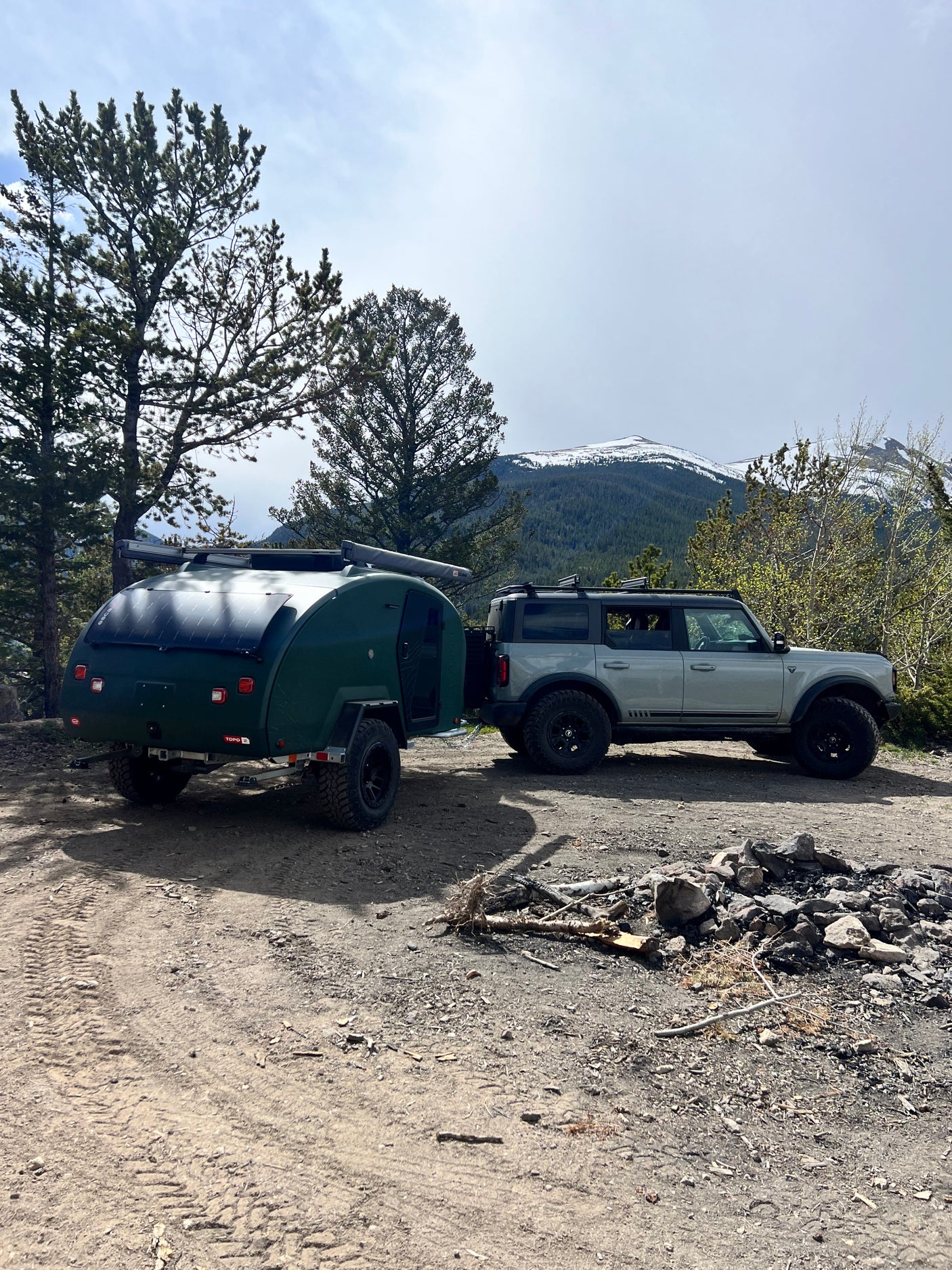 Explore with this RV rental: Grey Ford Bronco towing a green teardrop camper at a mountain campsite.