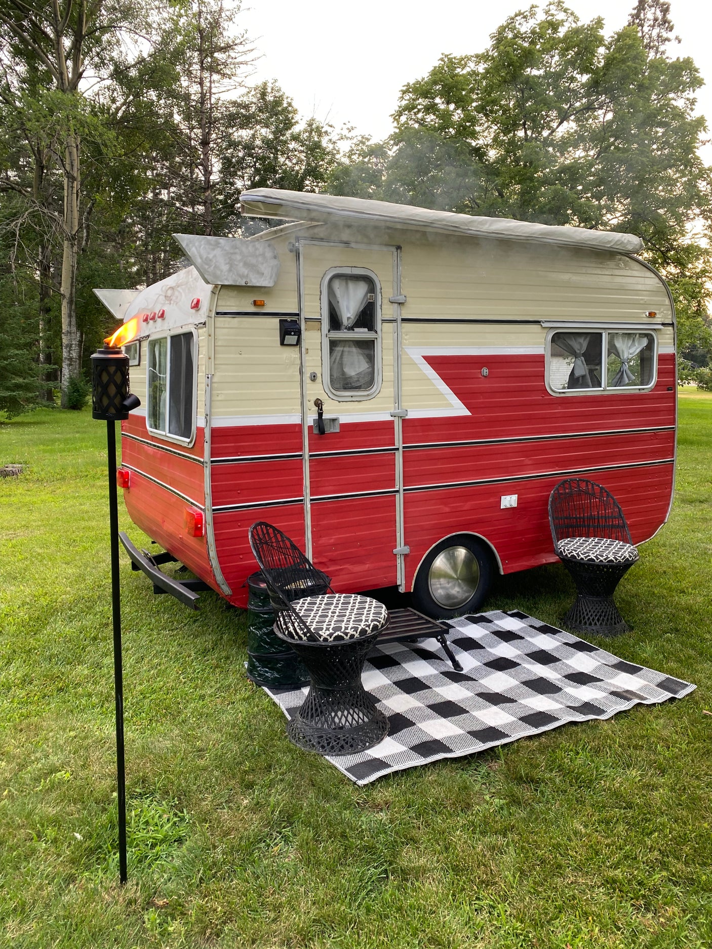 This charming vintage **RV rental** offers an inviting outdoor space with chairs, a checkered mat, and a tiki torch.