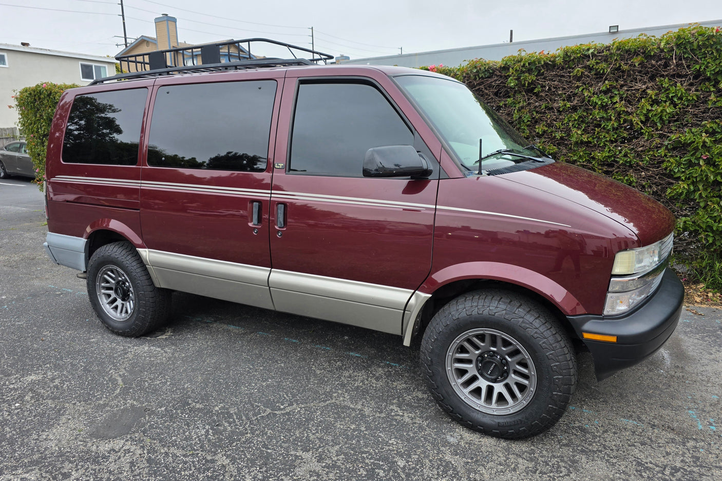 Maroon and tan Chevy Astro van, equipped with a roof rack and all-terrain tires. Perfect for your next RV rental adventure.