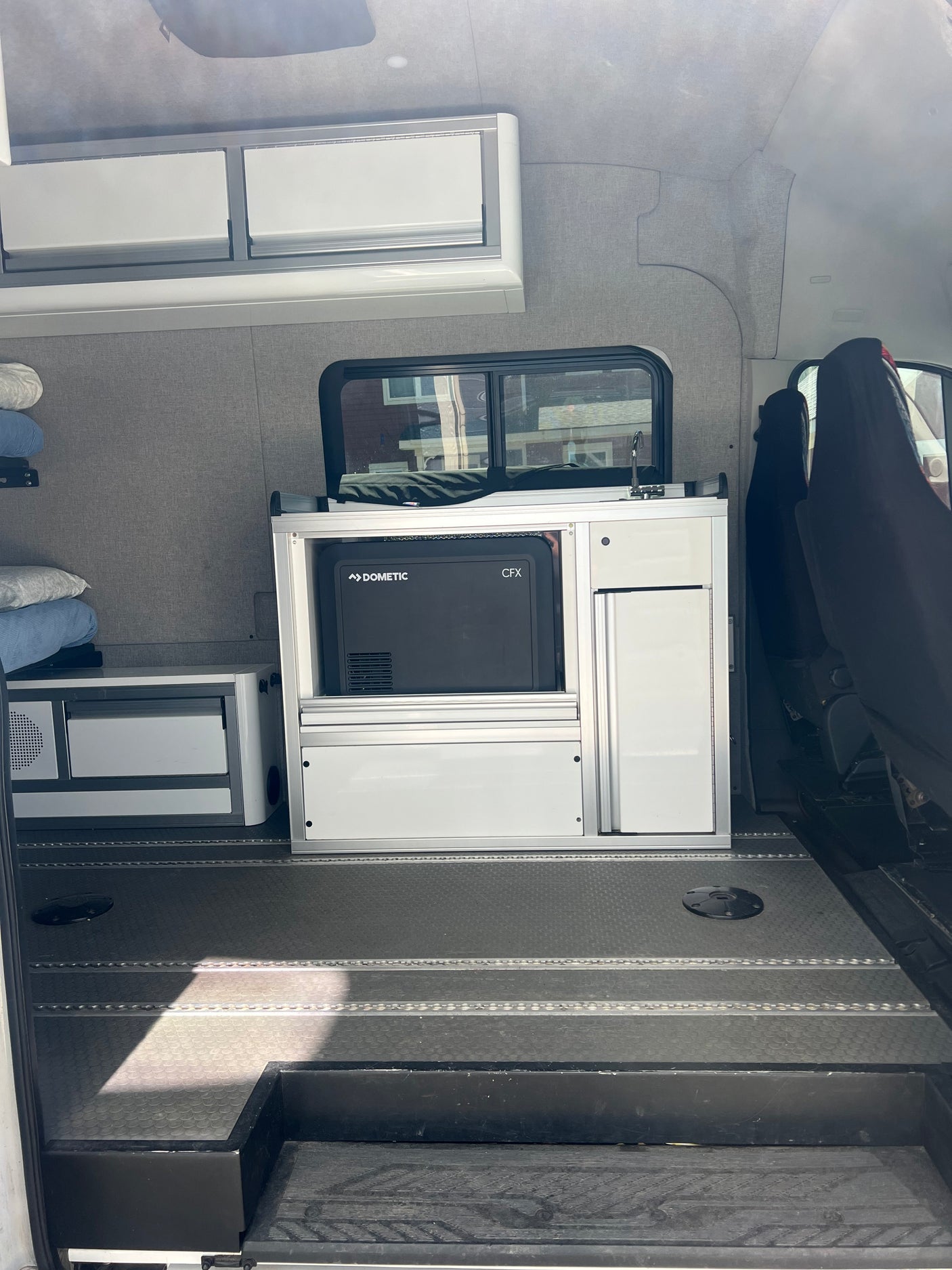 RV rental interior: A Dometic fridge built into white modular storage, alongside upholstered grey walls & textured floor.