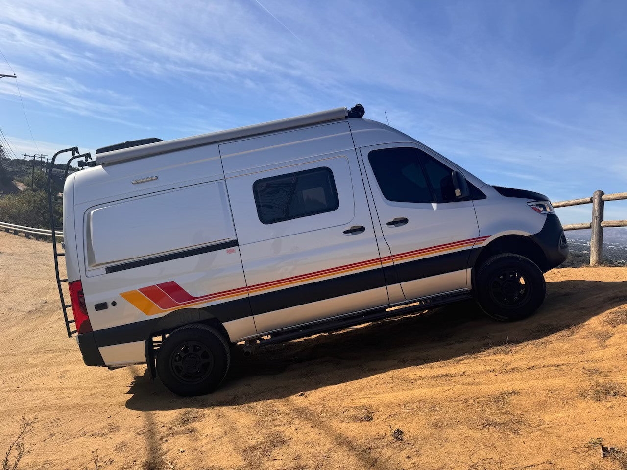 A silver off-road camper van, ideal for rv rental, angled on a dirt hill with scenic views. Adventure awaits!