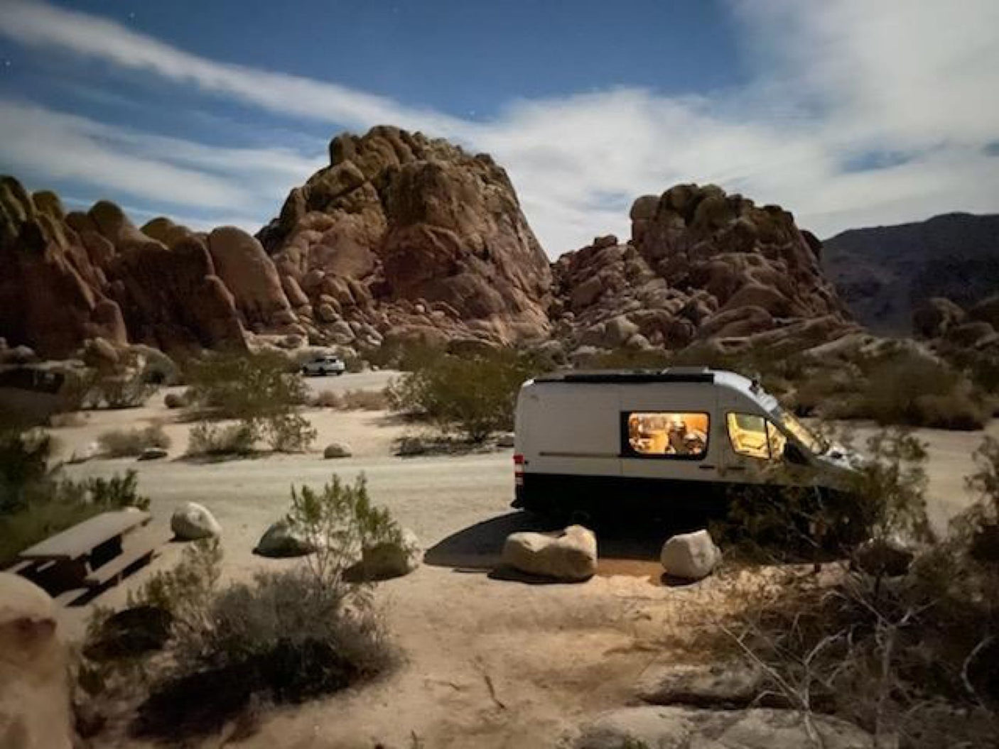 Night camping adventure: RV rental parked among desert rocks under a moonlit sky, interior lit. Perfect for travel.