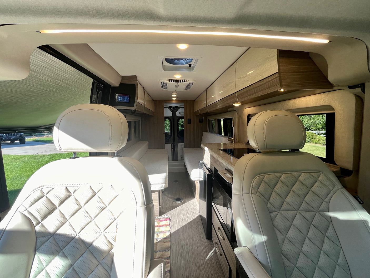 Spacious RV rental interior with cream quilted seats, modern kitchenette, and bright ceiling lights for ultimate travel comfort.