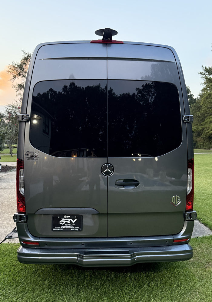 surrounded by green grass and trees.|This grey RV rental van features a large "Let's Go Aero" rear cargo box