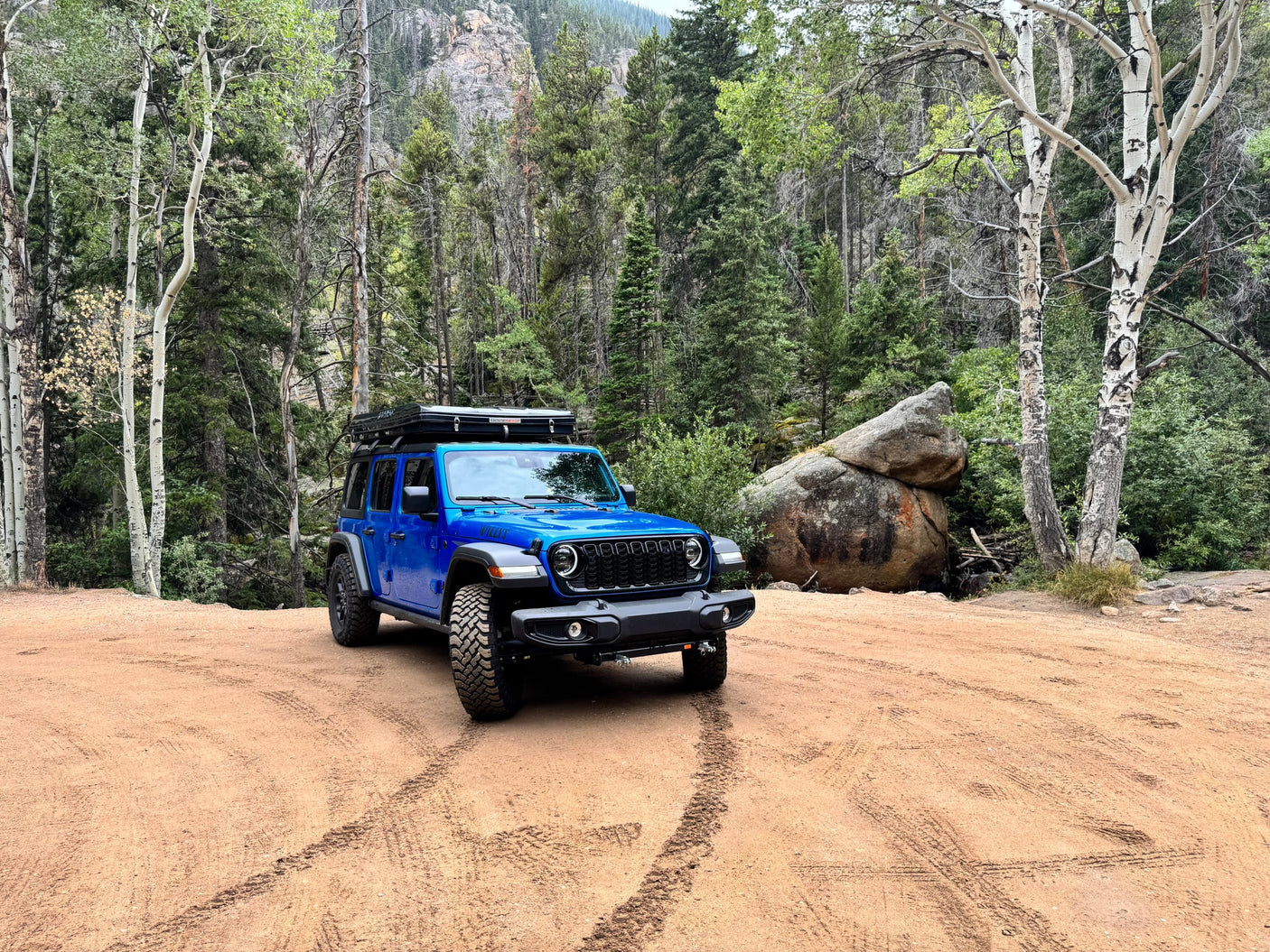 A vibrant blue Jeep Wrangler with a rooftop tent, offering an RV rental alternative for exploring the mountain forest.