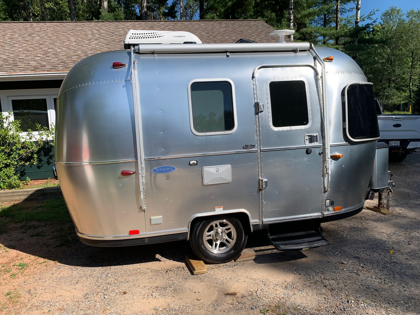 A sleek silver Airstream travel trailer, perfect for an RV rental, is parked on a gravel lot under a clear sky.