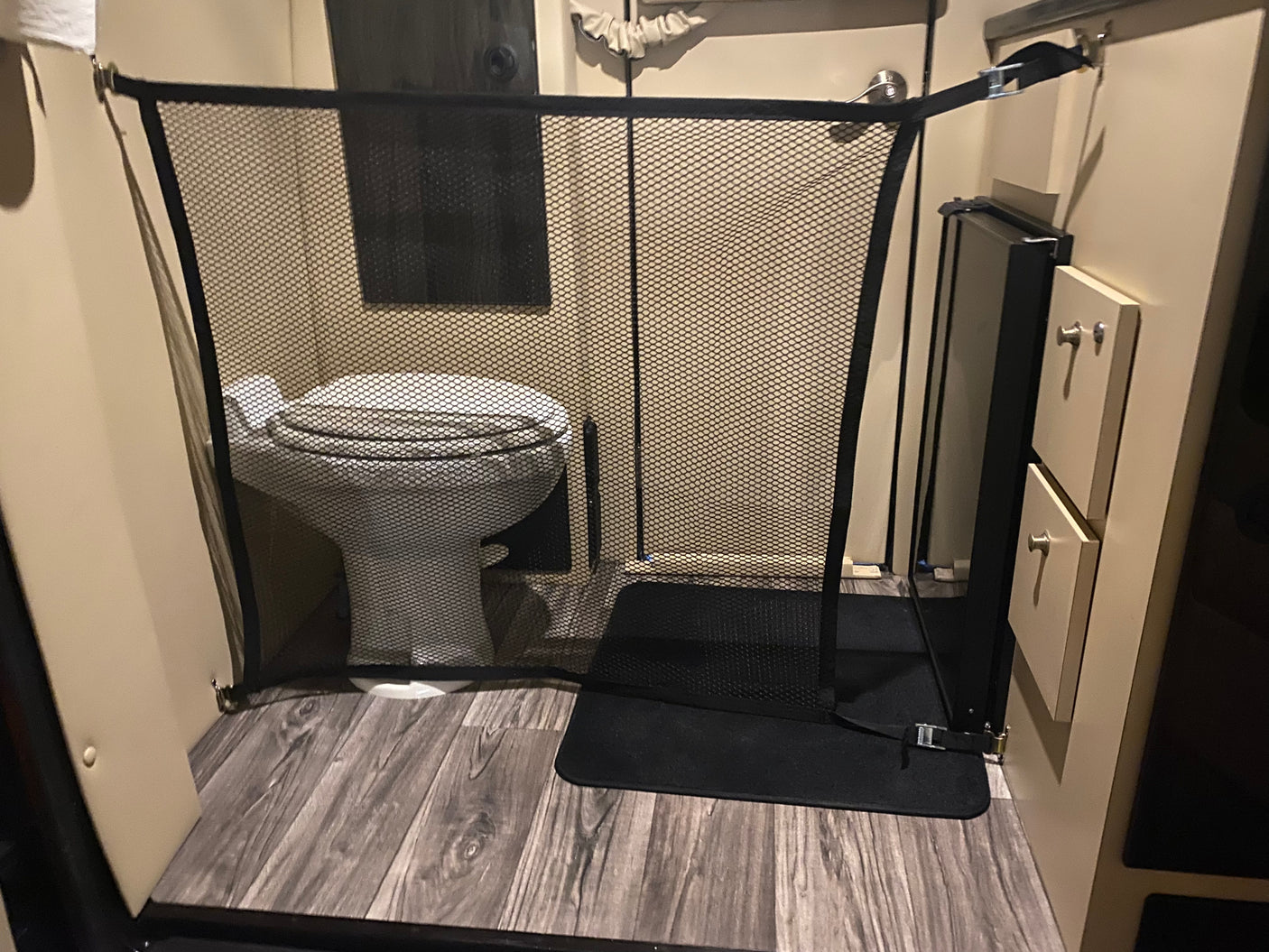 RV rental bathroom showing a toilet blocked by a black mesh pet gate on wood-look floors. Ideal for keeping pets out.