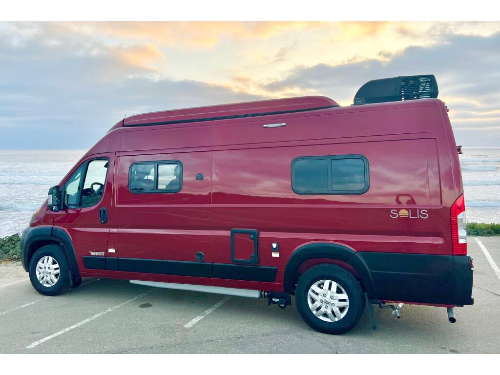 This red Winnebago Solis RV rental is parked by the ocean, ready for scenic road trips and coastal adventures.