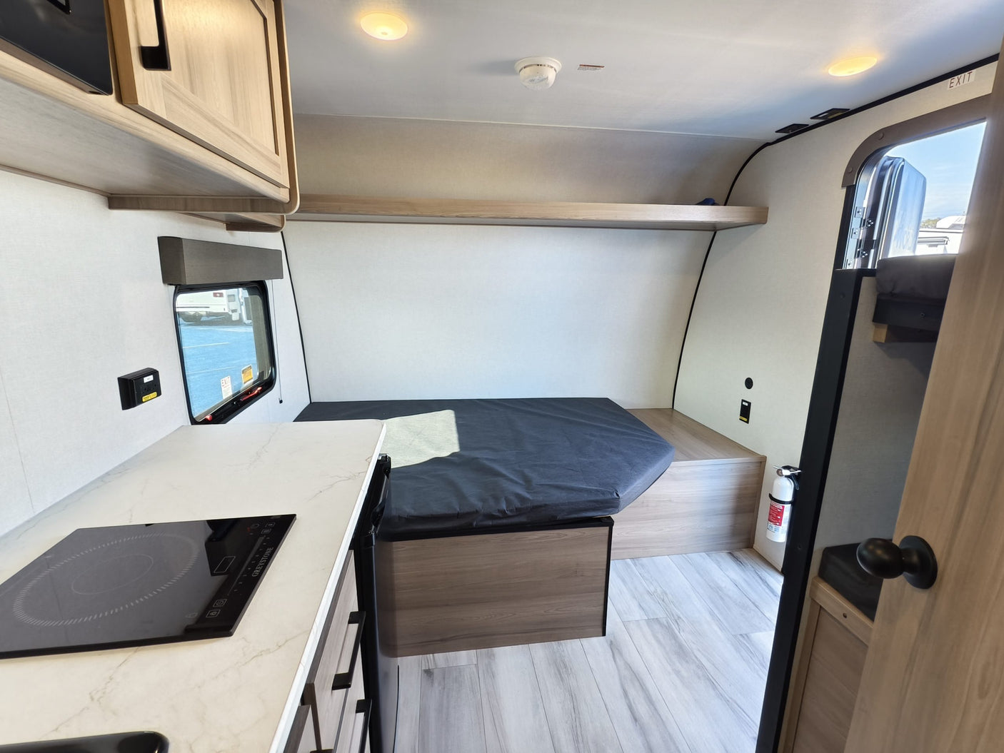 Compact RV rental interior featuring a kitchen with cooktop, sleeping area, and overhead storage, ideal for adventure.