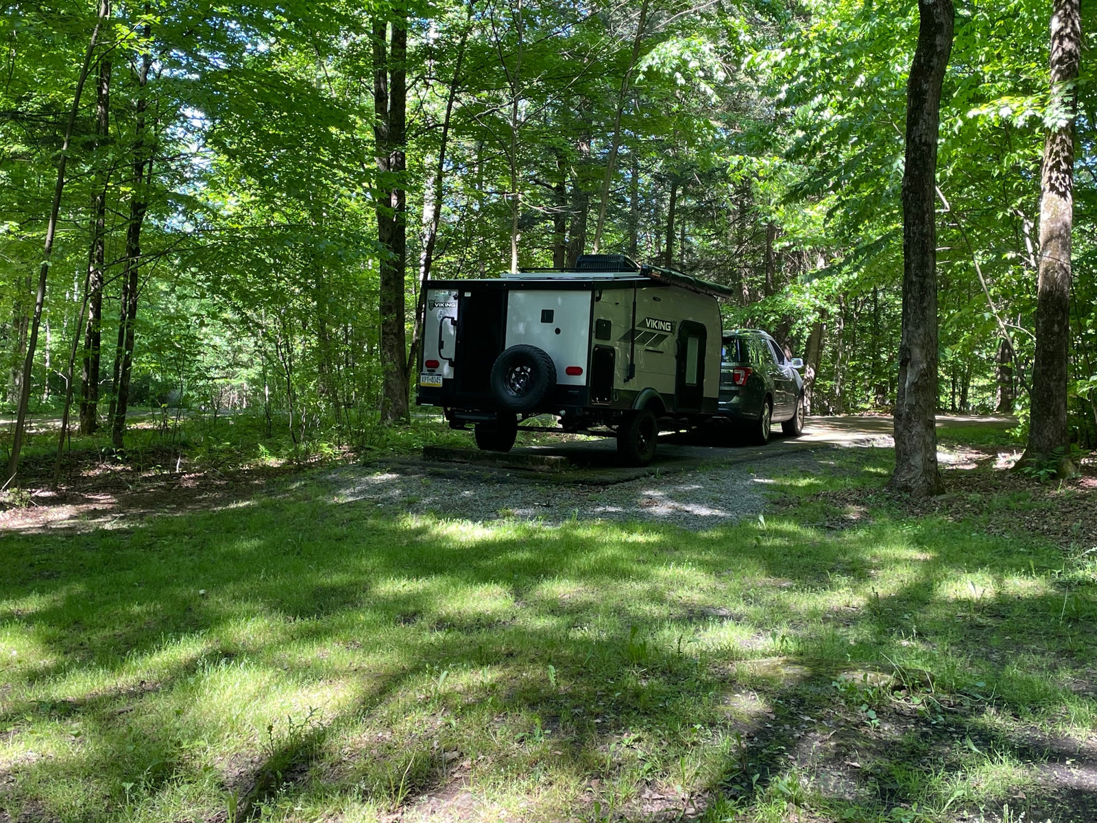 A Viking travel trailer RV rental, towed by a truck, sits in a sunlit forest campsite.