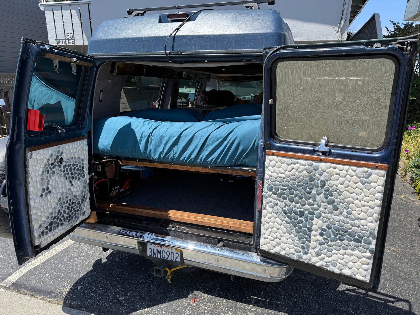 Step into this custom camper van conversion, an RV rental with a comfy bed, under-bed storage, and unique pebble-tiled doors.