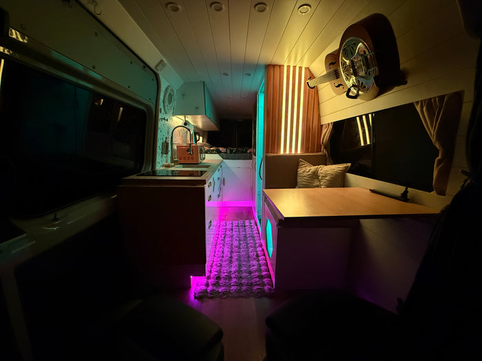 Cozy rv rental interior featuring a kitchen area, dining nook, wall-mounted guitar, and vibrant custom LED lighting.